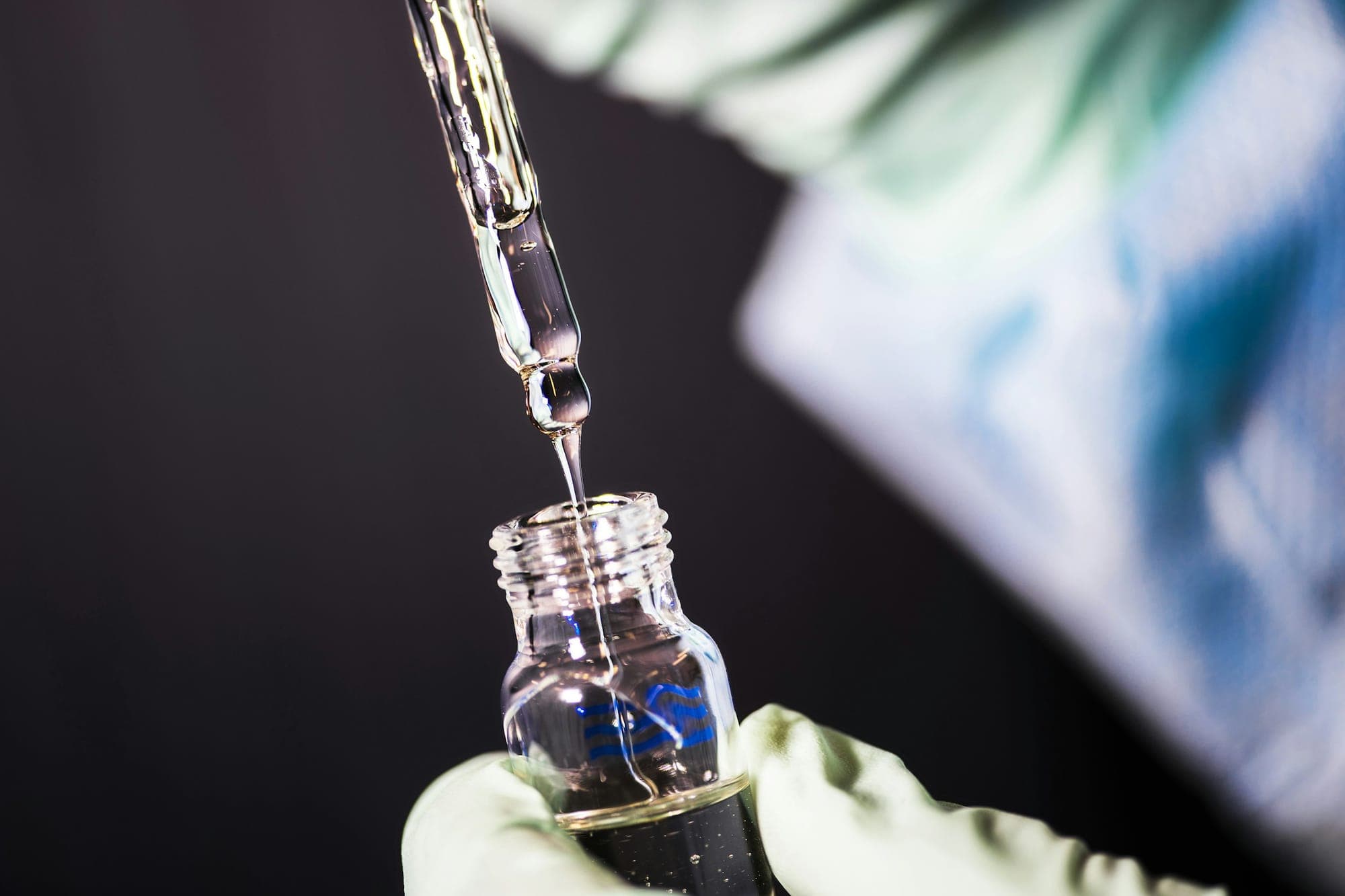A gloved hand dripping liquid from a pipette into a vial